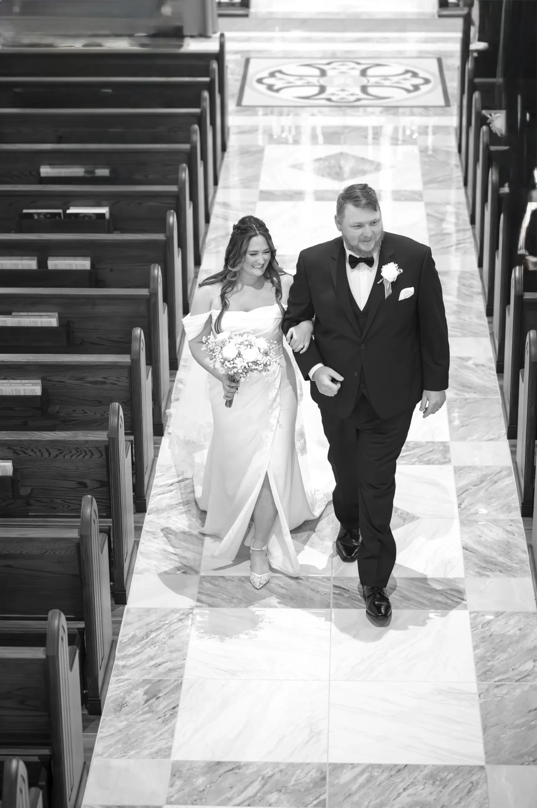 Virginia walking down the aisle hand in hand with James, smiling in her Serendipity Bridal gown.