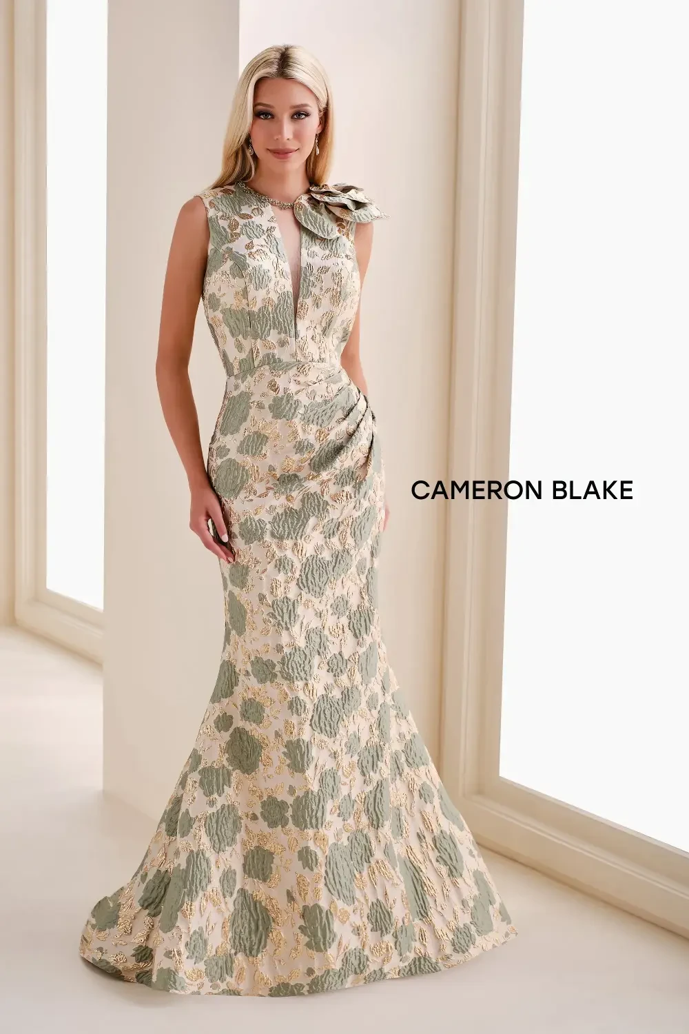 A model wearing a floral evening gown standing in a well-lit room.