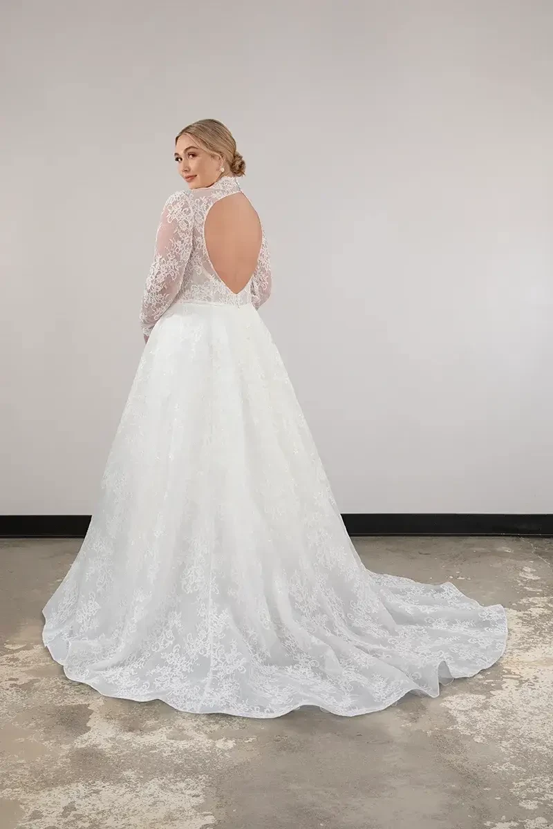model is wearing a plus size high neckline ball gown wedding dress with an open back