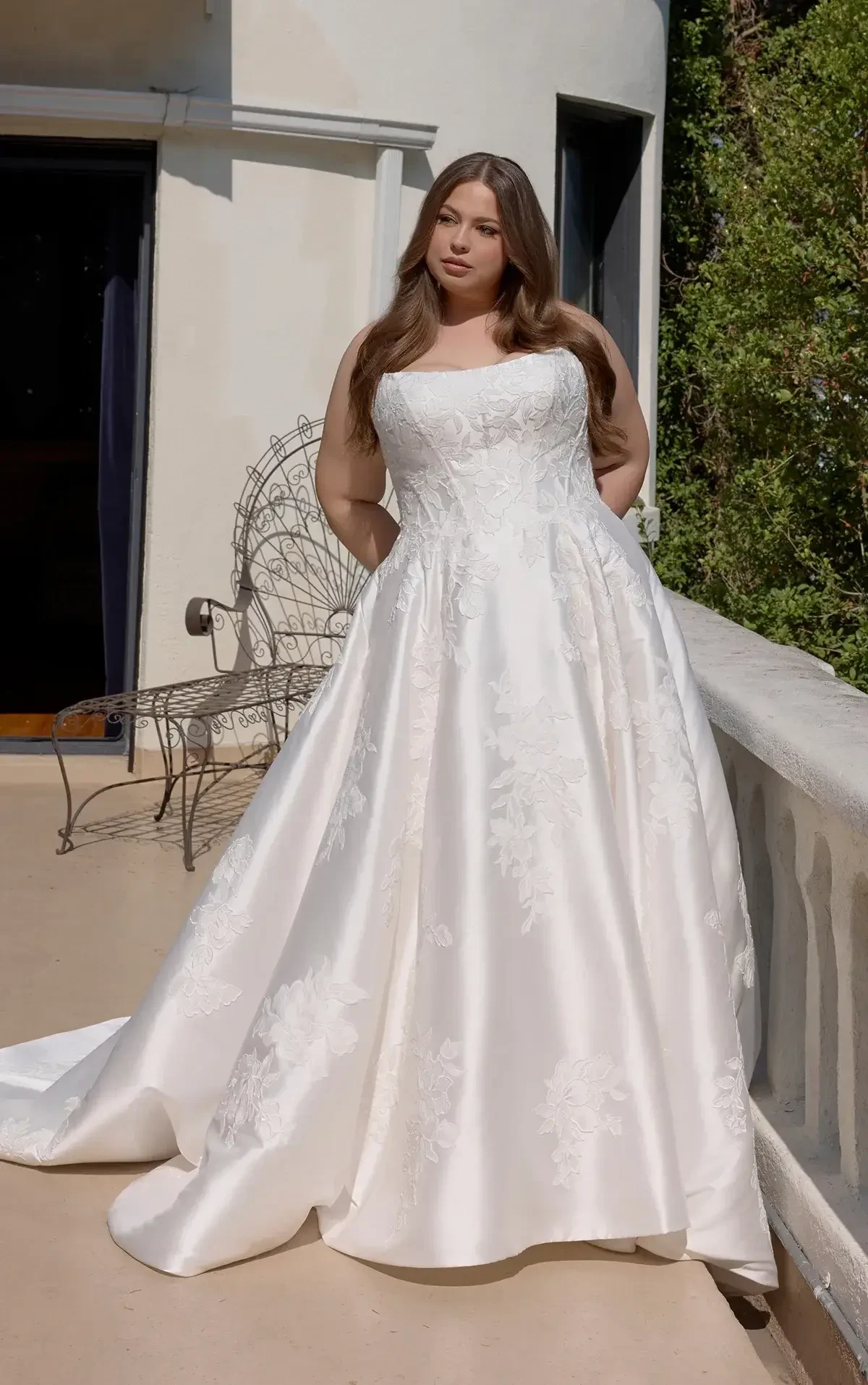A woman wearing a strapless, white wedding dress standing on a balcony.