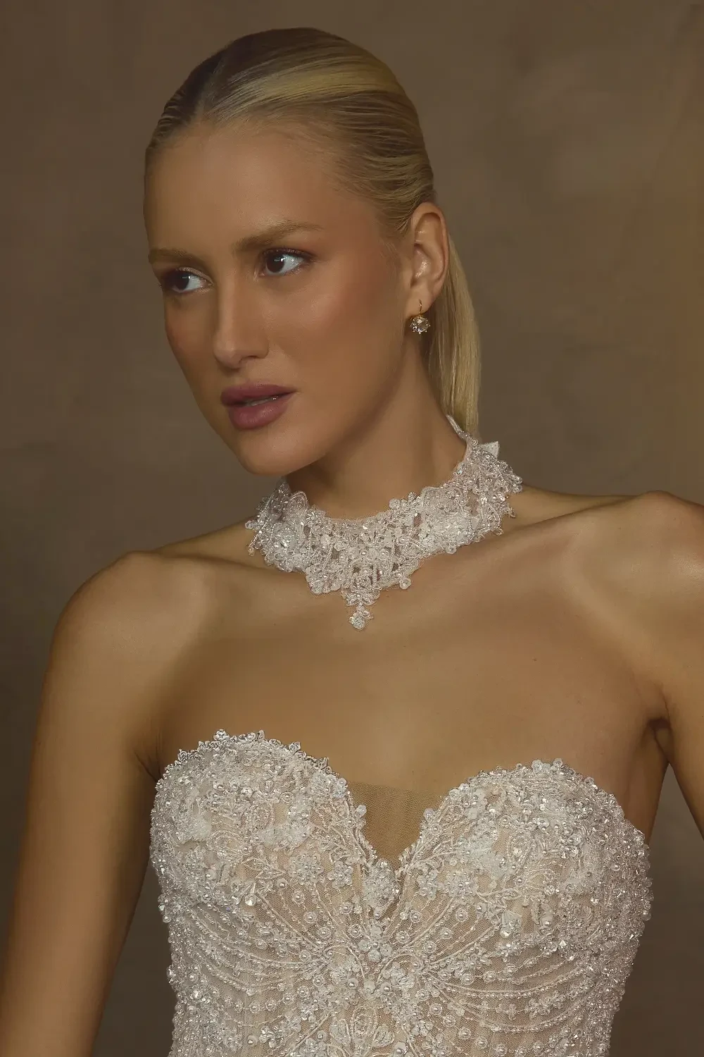 Woman wearing a detailed, strapless bridal gown with intricate beading and a matching lace choker.